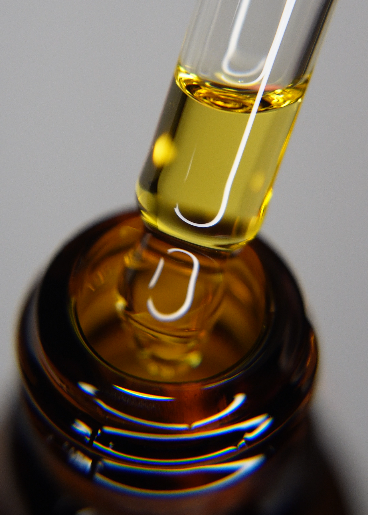 Close-up of a glass dropper with yellow liquid on a dark background